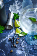 Summer alcoholic cocktail blueberry mojito with rum, mint, lime and ice, bar tools, gray background, selective focus