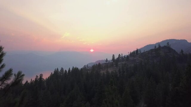Forest Fire Sunset. Smoke of wildfires in the air creating amazing sunset pink, red, orange sky. Smoke blanketing the hills in the background. Drone aerial shot over tree tops showing distant lake
