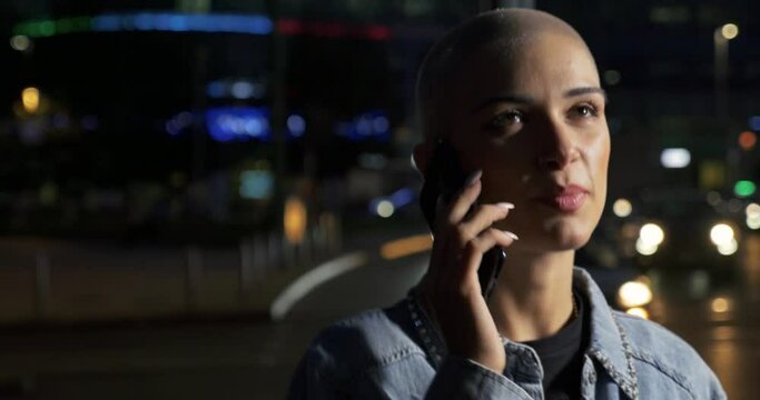 young woman using mobile phone on the street. Girl with short shaved hair walking in the evening in the city center