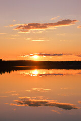 Obraz premium Sunset with strong colors. Lake, horizon, orange sky with cloudlets, glowing sun and reflection. Kemijärvi Finland.