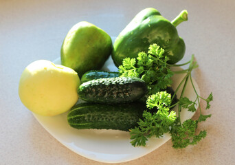 Fresh vegetables and fruits - Apple, cucumber, pepper, parsley - on a white saucer on a gray kitchen table, close - up-the concept of proper healthy nutrition