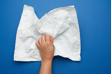 woman holds in her hand a crumpled sheet of paper in a cage on a blue background