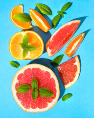 Concept lots of juicy slices of grapefruit, oranges and green Basil on a bright blue paper background