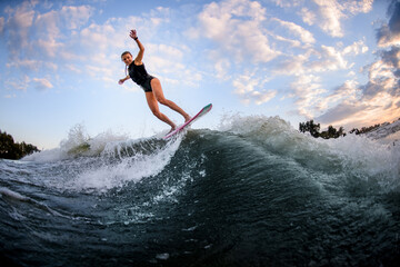 Fototapeta na wymiar Active girl in swimsuit jumping up on surf style wakeboard against blue cloudy sky