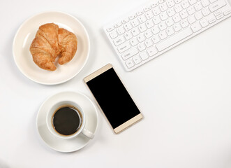 flat lay of blank screen mobile phone, coffee cup ,croissant ,computer keyboard on white background with copy space. Morning working time concept.