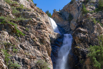 Obraz premium Burkhan bulak waterfall, the highest waterfall in Kazakhstan. Waterfall with strong stream is flowing among rocky mountains. Outdoor landscape. Tourism in Kazakhstan concept. Summer vacation concept.