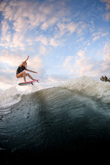 beautiful view of woman jumping over big splashing wave on surf style wakeboard.