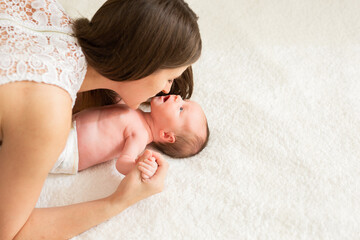 Home portrait of newborn baby with mother on bed. Mom holds and kisses her baby. 
Mother with child