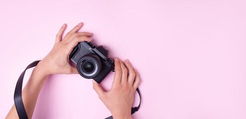 Hands hold a black camera on a pink background. View from above