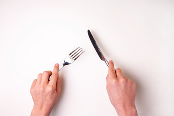 Hands hold a knife with a fork on a white table isolated. View from above