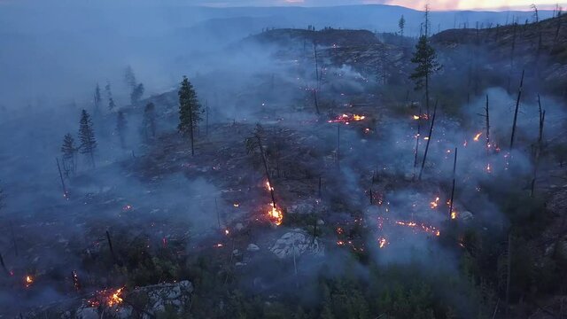 Wild fire burning and flames in 4k drone shot. BC British Columbia Okanagan valley at twilight or dawn. Flames, glow, blaze and smoke over dead woods and trees