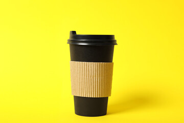 Takeaway paper coffee cup with cardboard sleeve on yellow background