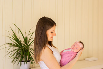 Naklejka premium Home portrait of newborn baby with mother on bed. Mom holds and kisses her baby. Mother with child