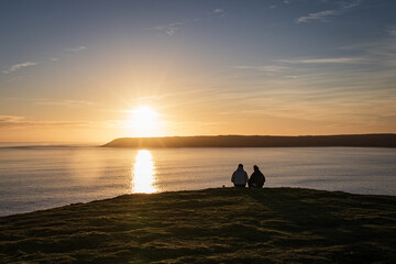 Naklejka na ściany i meble People watching sunset at Rhossili Bay, Worm's head, Gower Peninsula beach, Swansea, Wales, United Kingdom, Europe