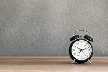 Black metal retro alarm clock on wooden desk with concrete wall on the background