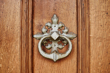 Old, rusty door knocker ornament on patterned, wooden door.