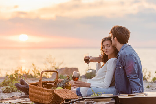Selective focus of couple holding glasses of wine during picnic on beach at evening - Powered by Adobe