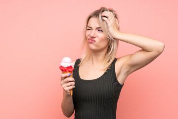 Young blonde woman with a cornet ice cream over isolated pink background having doubts and with confuse face expression