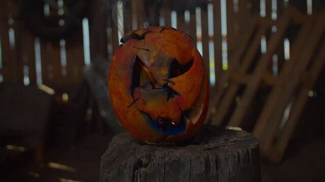 Close-up of scary spooky carved halloween pumpkin lantern with fire burning inside placing on wooden stump in dark creepy shed. Halloween and minimal holiday concept.