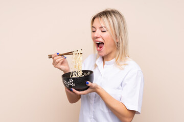 Young Russian woman over isolated background holding a bowl of noodles with chopsticks and eating it