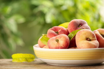 Fresh ripe donut peaches on wooden table against blurred green background, closeup. Space for text