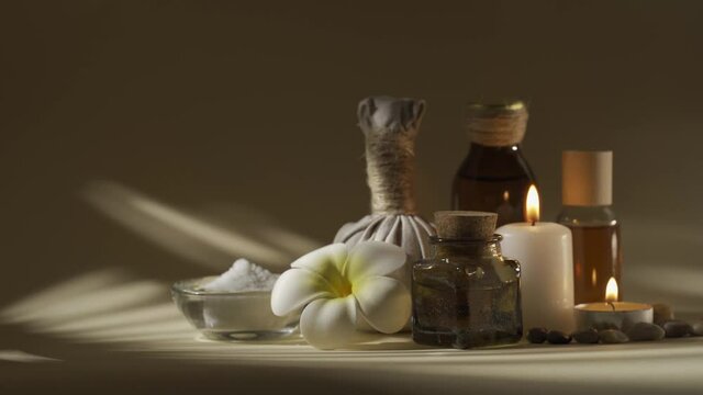 Beautiful spa composition with candles, frangipani flower, oil flasks, bowl with salt and herbal ball. No color grading
