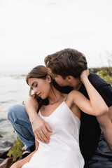Young man kissing girlfriend in dress on beach near sea