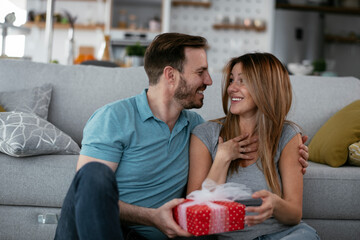 Husband surprising his wife with a gift. Young man giving gift box to his wife. - Powered by Adobe