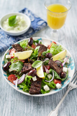 Tasty Salad with Grilled Beef Pieces, Cherry Tomatoes, feta Cheese and Kalamata Olives. Bright wooden background.