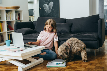 young girl using laptop, sitting on floor in her living room