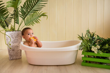 beautiful baby boy sitting in a bath and eating oranges on a wooden background