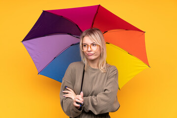 Young blonde woman holding an umbrella over isolated yellow wall thinking an idea
