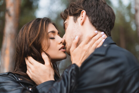 Selective focus of young couple in leather jackets kissing in forest