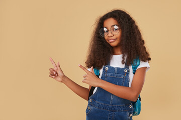 Smart ethnic schoolgirl pointing at blank space