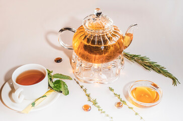 Fragrant fresh herbal tea and melissa in a glass teapot warming on a candle on a white table. Traditional herbal drink. Tea with honey in a restauran. Kettle warmer