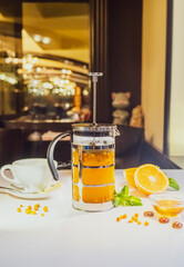 Tea in a teapot with physalis and honey on a white table against the background of the restaurant