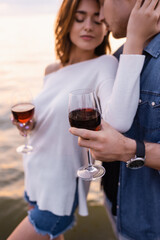 Selective focus of man holding glass of wine near girlfriend and sea