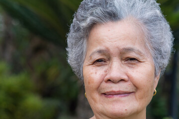 A close-up of an elderly Asian woman looking at camera while standing in a garden. Beautiful face of senior woman portrait. Concept of old people and healthcare