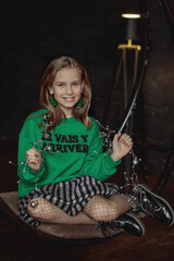 Portrait of a beautiful little girl in a fashionable New Year's image, in a green sweatshirt and with Christmas bulbs in her hands. Merry Christmas and Happy New Year.
