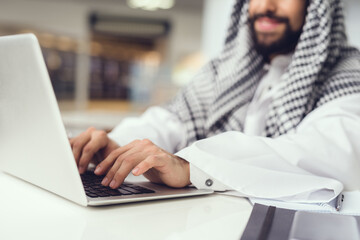 Young Arabian Man in Scarf Using Laptop in Cafe.