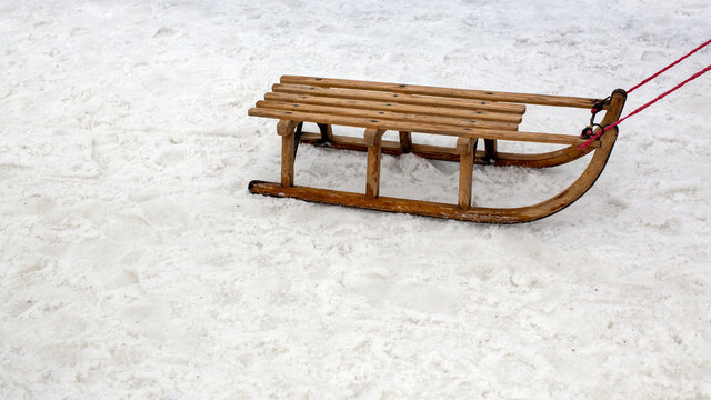 Holzschlitten wird an einem roten band &uuml;ber eine platt getrampelete Schneedecke gezogen- Konzept Winter
