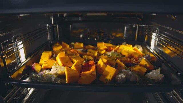 Sliced pumpkin with thyme, olive oil, salt, garlic and onion on dripping pan in oven