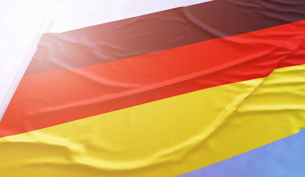 German flag on the blue sky. Close up national flag in bright rays sun that is waving in the wind on flagpole.