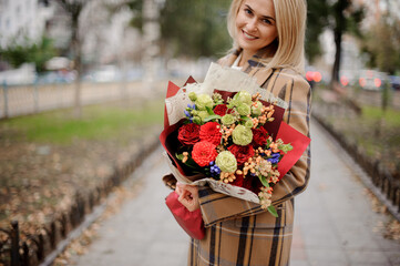 happy smiling young woman in park with bouquet of bright flowers in her hands