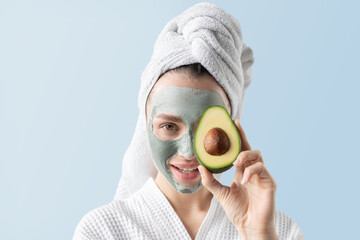 Close up portrait of young female in mask and white towel holding piece of avocado. Advertising poster of eco-friendly beauty products for healthy glowing skin. Skincare concept