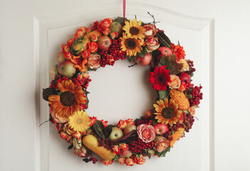 Beautiful autumnal wreath with flowers, berries and fruits hanging on white wooden door. Space for...