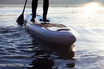 Close-up of male legs on paddle board (SUP) in water of the river at winter morning