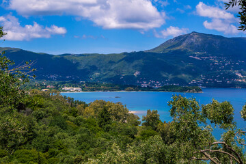 Naklejka na ściany i meble Beautiful summer landscape with sea bay with calm water, village and mountains on the horizon and clouds on blue sky.