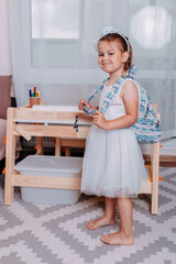 Little student with blue backpack near school desk. Back to school. Little girl studies at home.