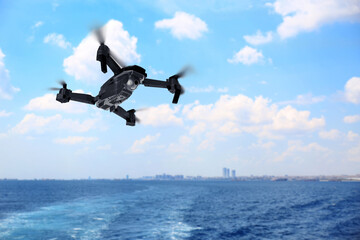 Modern drone flying over sea and blurred cityscape on background. Aerial survey